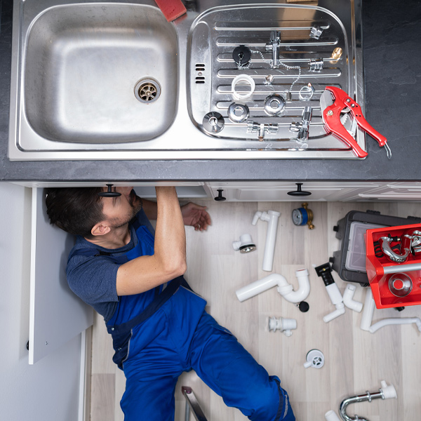 professional in blue uniform cleaning drain under sink