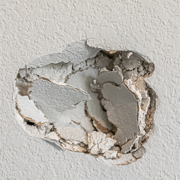 A hole in the wall of a hallways caused by a fist punching through the wall