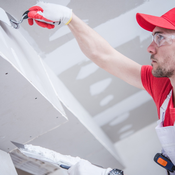 professional in red and white uniform doing drywall work