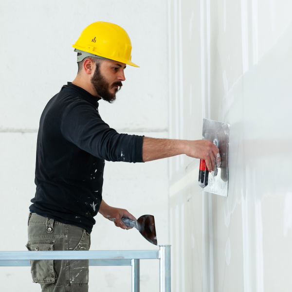 professional in black shirt and yellow work hat working on drywall project