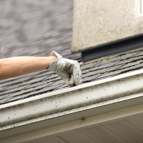 professional with glove on cleaning out gutter