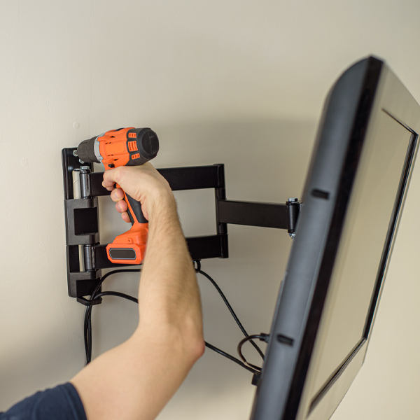 professional using orange drill to hang television