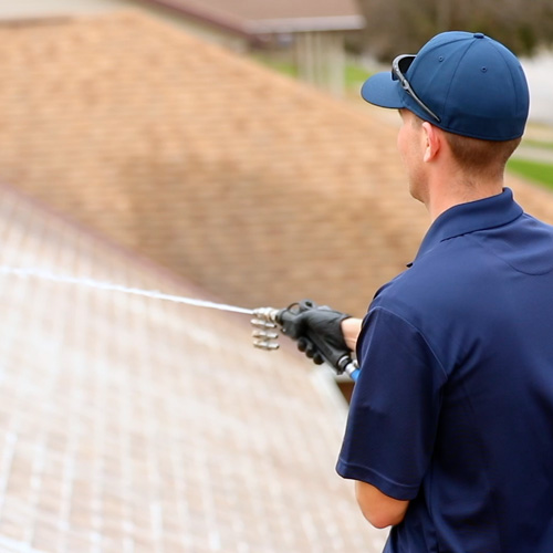 professional in blue hat and shirt spraying roof of home